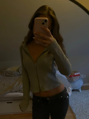 Grå ribbad kofta med dragkedja - Säljer en grå croppad hoodie med ribbad struktur och dragkedja framtill. Dragkedjan går att dra up både nerifrån och uppifrån. Tröjan har långa ärmar och en huva som ger en chill vibe. Perfekt för dig som gillar en avslappnad och snygg stil.