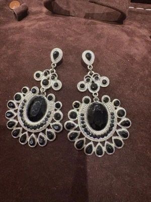 Stora svarta statementörhängen - Säljer ett par riktigt snygga statementörhängen i silverfärg med svarta stenar. De har en droppformad design med massor av detaljer och gnistrande svarta stenar runt en stor oval mittsten. Perfekta för dig som vill sticka ut och addera lite edge till din look.