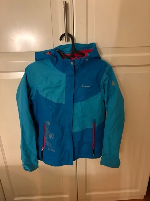 Blå vindjacka från Icepeak med blommor - Jag säljer denna super snygga blåa vindjackan från Icepeak med fina blommiga detaljer och rosa dragkedjor. Jackan har huva, lång ärm och är gjord i polyester. Köp nu jag postar snabbt!!💗💕