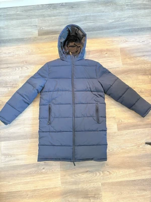 Mörkblå lång pufferjacka Selected Homme - Säljer en helt ny mörkblå pufferjacka från Selected Homme med huva och två fickor med dragkedja. Jackan är lång, har raka linjer och quiltad design. Perfekt för kalla dagar och har en clean look som funkar till alla stilar. Den är för man men passar tjejer lika väl. Nypris för denna är 1500 och nu 300kr!! Hör gärna av dig för fler bilder eller frågor 
