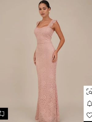 Lång spetsklänning i ljusrosa - Romantisk långklänning i ljusrosa spets med volangdetaljer vid axlarna och snörning i ryggen. Klänningen har figurnära passform och är ärmlös med breda axelband. Perfekt för bal eller student.