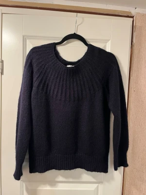 Mörkblå stickad tröja från Noa Noa - Mysig mörkblå stickad tröja från Noa Noa i storlek M. Tröjan har rund halsringning, ribbade muddar och trekvartslång ärm. Perfekt för kyliga dagar och enkel att matcha med jeans eller kjol. Ullmix