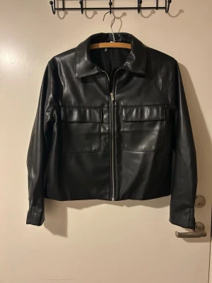 Svart läderjacka (stl M) - Denna läderjacka uppgraderar din garderob och tar dina outfits till en ny nivå!⭐️ Med det silkeslena veganska lädret och detaljerade sömmarna är det ett självklart val för dig som älskar mode!   (Modellen är unisex, den passar både kvinnor och män)   Tveka inte att höra av dig för vidare frågor🤗 