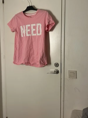 Rosa t-shirt från ONLY med tryck - Pris kan diskuteras och tvätt ingår innan leverans . Säljer en rosa t-shirt från ONLY i storlek L med stort vitt tryck där det står 'NEED' på bröstet. T-shirten har klassisk rund hals, korta restyle-ärmar och är mixad i en mjuk bomullskvalitet. Perfekt för en chill och avslappnad look.