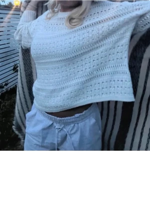 Vit stickad tröja med hålmönster - Säljer en vit stickad tröja med snyggt hålmönster och rund hals. Tröjan har en lite croppad passform och långa ärmar med ribbade muddar. Perfekt att slänga på sig under kyliga dagar för en chill och stilren look.