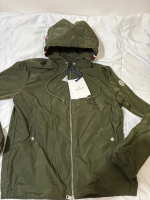 Moncler grimpeurs windbreaker jacka i grön  - Säljer en klassisk Moncler Grimpeurs vindjacka i mycket fint skick. Jackan är mörkgrön och har den ikoniska trikoloren längs luvans kant samt Moncler-loggan på vänster ärm.