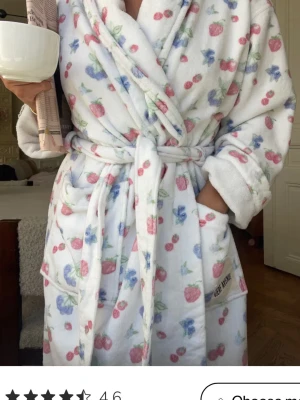 Vit morgonrock med bärmotiv - Supermjuk vit morgonrock från Djerf avenue, med sött mönster av blåbär och jordgubbar i blått och rött. Modellen har knytskärp i midjan, stora fickor och en klassisk krage. Perfekt för chilliga morgnar eller kvällar hemma. ALDRIG ANVÄND