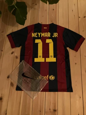 Barça Neymar Jr #11 Nike fotbollströja - Säljer en FC Barcelona matchtröja från Nike i storlek M med Neymar Jr och nummer 11 på ryggen. Tröjan har klassiska blå och vinröda ränder, gula detaljer och klubbmärke på bröstet. Materialet är lätt polyester med Dri-FIT teknologi för extra komfort. Inte riktig men jättebra kvalite