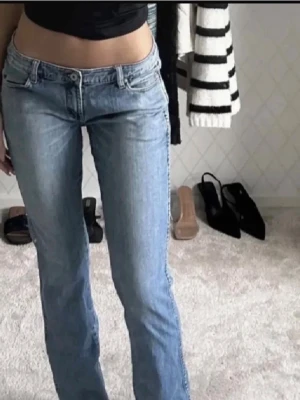 TBY ljusblå bootcut jeans - Säljer ett par ljusblå jeans från Replay med klassisk femficksdesign och snygga detaljer på bakfickorna. Modellen har låg midja och bootcut. Står stl 34 i byxorna men skulle säga att de passar M/38.