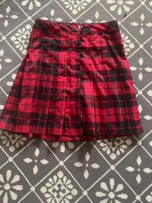 Rutig röd kortkjol - Säljer en röd och svart rutig kortkjol från Kappahl i storlek 170. Kjolen har knapp och dragkedja i midjan.