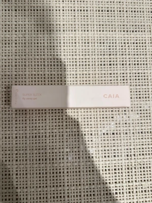CAIA Super Sleek fly away gel - Super Sleek fly away gel från CAIA i en stilren ljusrosa förpackning. Perfekt för att hålla småhår och babyhår på plats. Kommer i en smidig, avlång kartong med diskret text. Enkel att ta med i väskan och använda när som helst.