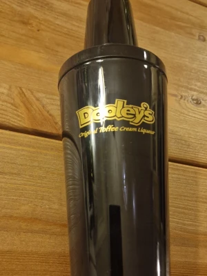 Svart Dooley's cocktailshaker - Säljer en svart cocktailshaker från Dooley's med guldfärgad logga och måttskala på sidan. Shakern är i plast och har tre delar: lock, sil och behållare. Perfekt för att blanda drinkar hemma och enkel att använda. Höjd på alla delar ihopsatt är ca 23 cm. Den är oanvänd men tagen ur förpackning för att stå i drinkskåpet.