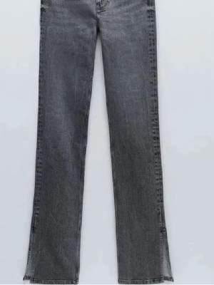 Grå bootcut jeans med slits - Snygga grå jeans med bootcut-snitt och slits vid bensluten. Jeansen har klassisk femficksdesign och är tillverkade i ett stretchigt denim-material som sitter skönt. Perfekt för dig som gillar en trendig och avslappnad look.
