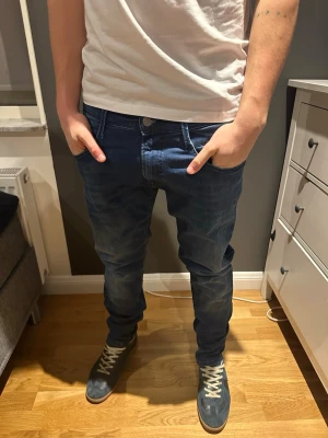 Replay Anbass jeans blå strl 33 - Snygga Replay Anbass jeans i klassisk blå färg. Modellen har normal passform med raka ben och fem fickor. Jeansen är tillverkade i mjukt denim-material och har en stilren look med Replay-logga på bakfickan och läderpatch i midjan.