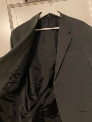 Olivgrön kavaj från Zara - Stilren svart kavaj från Zara med klassisk passform och två knappar framtill. Fodrad insida i blankt tyg och tre fickor på framsidan. Perfekt för dig som vill ha en enkel och snygg look.