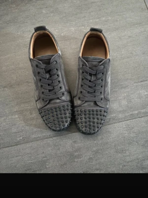 Christian Louboutin - Säljer ett par grå sneakers i mocka från Christian Louboutin skor i hyfsat skick. 8-9/10. De kommer med allt originalt som 2 dustbags, 2 kassar, extra skosnören, extra nitar. Har kvittot om de skulle behövas och kan gå ner i pris om det går snabbt.