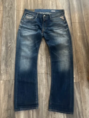 Blå Replay jeans straight fit - Säljer ett par blå jeans från Replay med klassisk straight fit och snygga slitningar framtill. Jeansen har fem fickor, orange kontrastsömmar och en cool vintage look. Perfekta för dig som gillar en avslappnad stil.