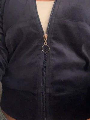 Mörkblå zip hoodie i velour - Snygg mörkblå hoodie i mjuk velour med dragkedja och rund metallring som zip puller. Hoodien har fickor framtill och ribbade muddar i nederkant. Perfekt för en chill och avslappnad stil. Dragkedjan är dock lite rostig men det är inget man lägger märke till 