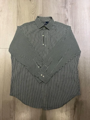 Grön randig skjorta Polo Ralph Lauren - Snygg grön och vit randig skjorta från Polo Ralph Lauren, modell Regent Classic Fit. Skjortan har klassisk krage, långa ärmar med manschett och vita knappar framtill. Perfekt för dig som gillar stilrena och tidlösa plagg med en fräsch vibe.