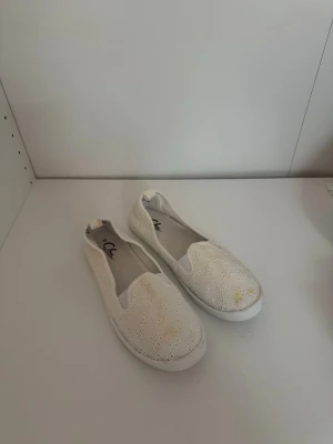 Vita ballerinaskor med broderade blommor - Säljer ett par vita ballerinaskor från Clou med broderade blommor och rund tå. Skorna har en platt sula och är tillverkade i bomull, vilket gör dem både lätta och luftiga. Perfekta för dig som gillar en söt och enkel stil. Har en del missfärgningar därav billigt pris✉️