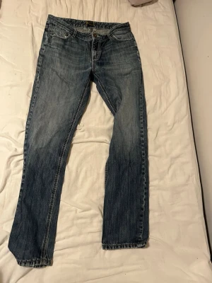 Levi's 501 blå jeans straight fit - Klassiska blå Levi's 501 jeans med rak passform och femficksdesign. Jeansen har en tidlös tvätt och subtila slitningar, perfekt för en avslappnad look. Tillverkade i robust denim med knappgylf och snygga detaljer på bakfickorna.