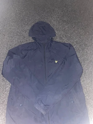 Marinblå jacka från Lyle & Scott - Snygg marinblå jacka från Lyle & Scott med meshfoder och klassisk design. Perfekt för dig som vill ha en stilren och enkel jacka med diskreta detaljer. Passar till många olika outfits och har en sportig känsla. Nackdel: vänster ficka saknar knapp. 