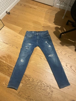 Replay hyper flex  - Säljer ett par blå skinny jeans från Replay med slitna detaljer och hål på benen. Klassisk femficksmodell med Replay-logga vid fickan och snygg tvätt. Jeansen har smal passform och är tillverkade i stretchig denim för extra komfort.