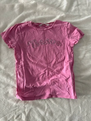 Rosa t-shirt med Brave-tryck H&M - Säljer en rosa t-shirt från H&M med texten 'Brave' i ett coolt tryck på bröstet. T-shirten har rund hals och korta ärmar, perfekt för en avslappnad och trendig look. Tillverkad i mjuk bomull som känns skön mot huden.