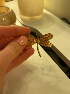 Guldfärgad ring med trollslända - ring i guldfärgad metall formad som en trollslända. Ringen har detaljerade vingar och en lång kropp som ger ett statement-utseende. Perfekt för dig som gillar djurmotiv och vill sticka ut med accessoarerna.