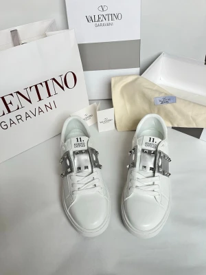 Vita sneakers Valentino Garavani - Snygga vita sneakers från Valentino Garavani med coola silverfärgade nitar och detaljer på sidorna. Skorna har snörning och är tillverkade i slätt skinn med en chunky sula. Perfekta för dig som vill sticka ut med exklusiv design.