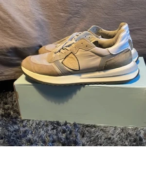 Beige sneakers från Philippe Model - Snygga beige sneakers från Philippe Model med detaljer i mocka och skinn. Skorna har rund tå, platt sula och klassisk snörning. Perfekta för dig som gillar stilrena och neutrala färger. Box ingår ej!