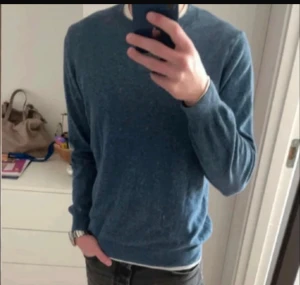 Merinoull tröja från Oscar Jacobson - Säljer en snygg blå stickad tröja från Oscar Jacobson. Tröjan har rund halsringning, ribbade muddar och är långärmad. Perfekt för dig som gillar klassisk och stilren look. Tillverkad i Italien.