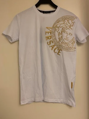 T-shirt med mönster  - Helt ny vit T-shirt med mönster. Är lite stenar på mönstret. Även detalj på sidan av T-shirten nertill. Även text på ena ärmen. Kan skicka fler bilder, så man ser trycket på nära håll. Lapp kvar.