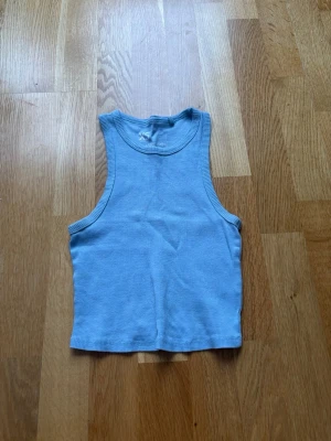 Ljusblå ribbad linnetopp - Säljer en ljusblå ribbad linnetopp med rund halsringning och ärmlös design. Toppen är croppad och har en enkel, clean look som passar perfekt till jeans eller kjol. Materialet är mjukt och stretchigt för en bekväm passform. Säljer på grund av för liten i storlek och kommer inte till andvänding!