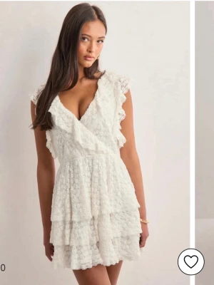 Vit spetsklänning med volanger - Supersöt vit klänning i spets med volanger längs axlar och kjol. Omlott framtill och öppen rygg med knytband upptill. Perfekt för sommarens alla tillfällen och ger en romantisk vibe. Använd en gång på skolavslutning. Klänningen säljs inte längre.