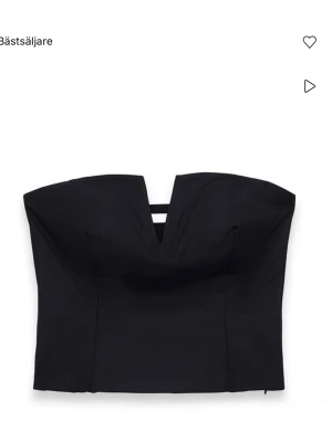 Svart axelbandslös korsettopp - Trendig svart korsettopp med axelbandslös design och en snygg v-formad urringning framtill. Toppen har en strukturerad passform och smockade partier baktill för extra komfort. Perfekt att styla med höga jeans eller kjol. Aldrig använd endast testad med lappen kvar.