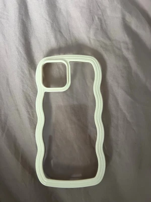 Ljusgult vågigt mobilskal till iPhone 12 - Snyggt mobilskal med vågig kant i ljusgult och transparent baksida. Skalets design har en unik form runt kameran och passar perfekt för dig som vill ha ett trendigt och stilrent skydd till din iPhone. iPhone 12