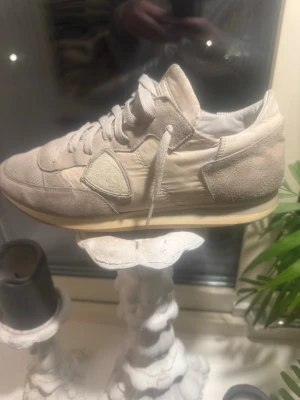 Beige Philippe Model sneakers - Snygga beige sneakers från Philippe Model med klassisk låg siluett. Skorna har snörning, rund tå och är tillverkade i en mix av mocka och textil. Diskret logga på sidan och tungan. Perfekta för dig som gillar stilrena och neutrala färger.