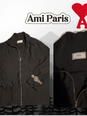 Svart jacka med dragkedja från Ami Paris - Stilren svart jacka från Ami Paris med hel dragkedja framtill och klassisk krage. Jackan har lång ärm och minimalistisk design, perfekt för en clean och modern look. Materialet känns lätt och smidigt, vilket gör den enkel att bära till många outfits.