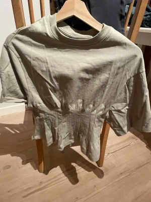 Militärgrön croppad topp med volang - Trendig militärgrön croppad topp med volangkant nedtill och rund hals. Tillverkad i mjuk bomull och har korta ärmar. Perfekt för dig som gillar en avslappnad men ändå stylish look.