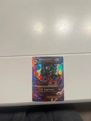 Pokémonkort M Rayquaza EX Full Art - Säljer ett holografiskt Pokémonkort av M Rayquaza EX med färgstark design och metallic-effekt. Kortet har attacken Dragon Ascent och är på engelska. Perfekt för samlare eller Pokémon-fans som vill utöka sin kortlek. Kommer från 2015