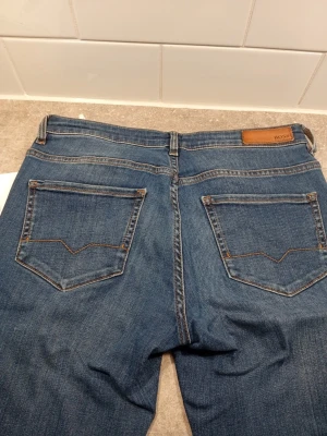 Blå jeans från Hugo Boss - Snygga blå jeans från Hugo Boss med klassisk femficksdesign och bruna kontrastsömmar. Jeansen har en läderpatch med BOSS-logga bak i midjan och raka ben. Perfekta för en stilren och avslappnad look. Storlek 27/32
