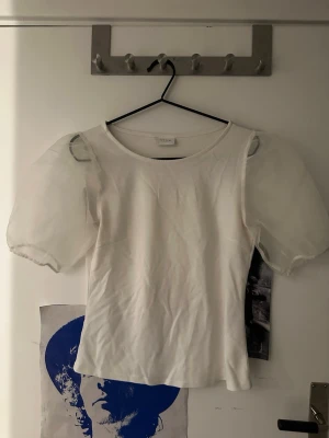 Vit topp med puffärmar  - Supersöt vit topp från Vero Moda med transparenta puffärmar i mesh och rund halsringning. Kroppen är i mjuk bomull och ärmarna ger en extra stylish touch. Perfekt att styla med jeans eller kjol för en trendig look. Den är insydd i midjan. Superfin! Knappt använd