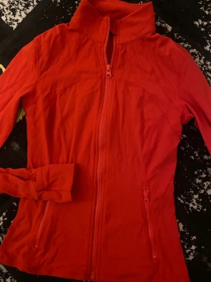 Röd tränings kofta  - Röd långärmad tränings kofta med krage och två fickor med dragkedja framtill. Helt oanvänd!