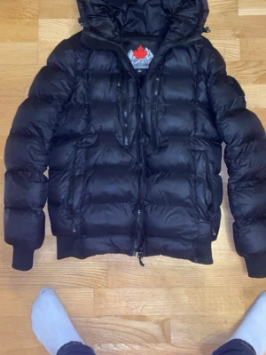 Svart dunjacka från Zaveti - Snygg svart dunjacka från Zaveti med huva och dragkedja framtill. Jackan har en quiltad design, två bröstfickor med dragkedja och ribbade muddar vid ärmsluten. Perfekt för kalla vinterdagar och ger en modern, puffer look. Lite tajtare model perfekt för dig som inte gillar när dina jackor flyger!💯💯💯