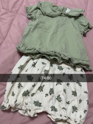 Grönt set med volang och blommiga shorts - Sött set med ljusgrön topp med volangkrage och volangkant samt vita shorts med grönt blommönster och resår i midja och benslut. Perfekt för en lekfull och avslappnad stil.