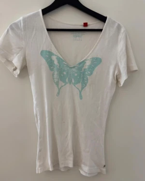 Vit t-shirt med fjäril från Esprit - Vit t-shirt från Esprit med ljusblå fjärilstryck och små silvriga pärlor på bröstet. Modellen har v-ringad hals och korta ärmar, jag har även sytt in den själv så nu passar den en s/xs. Mjuk bomullskvalitet och metallmärke med Esprit-logga vid nederkanten. Perfekt för dig som gillar detaljer och chill stil.