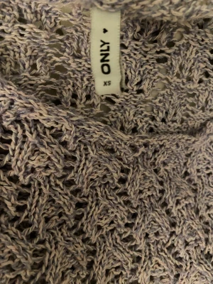 Ljuslila croppad stickad tröja ONLY - Säljer en ljuslila croppad stickad tröja från ONLY i storlek XS. Tröjan har ett snyggt hålmönster och trekvartsärmar, perfekt för dig som gillar en chill och trendig vibe. Materialet är mjukt och luftigt, och den har en vågig kant nedtill. 🎉