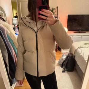 Dunjacka  - Säljer en beige pufferjacka från Cross sportswear med stor, mysig huva och svart dragkedja framtill. Jackan har två sidofickor och Cross sportswear logga på ärmen. Perfekt för kalla dagar. Jackan är i mycket bra skick, då jag knappt använt den. För att jag ångrade mig efter att retur och bytesrätten gått ut.  Säljer dels för det och för att jag vill spara ihop pengar till en annan jacka❣️Kontakta vid funderingar☺️