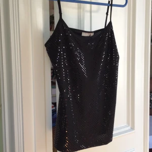 Svart paljettlinne från Lindex - Snyggt svart linne från Lindex med glittrande paljetter. Perfekt för en festlig kväll. Linnet har smala axelband och en elegant passform.